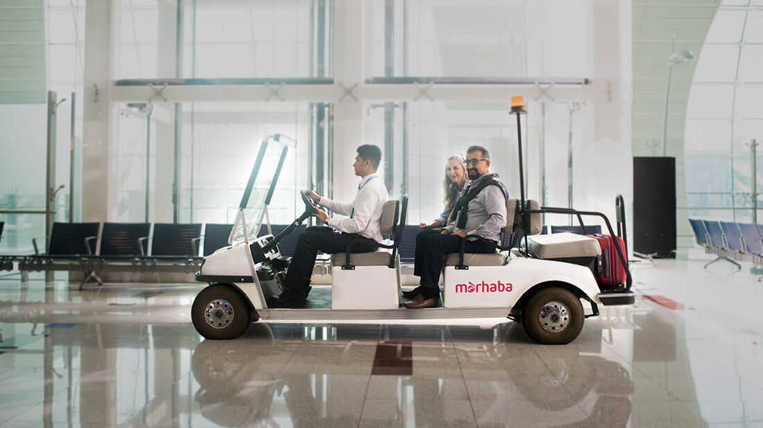 A couple being transported through the airport on a marhaba buggy
