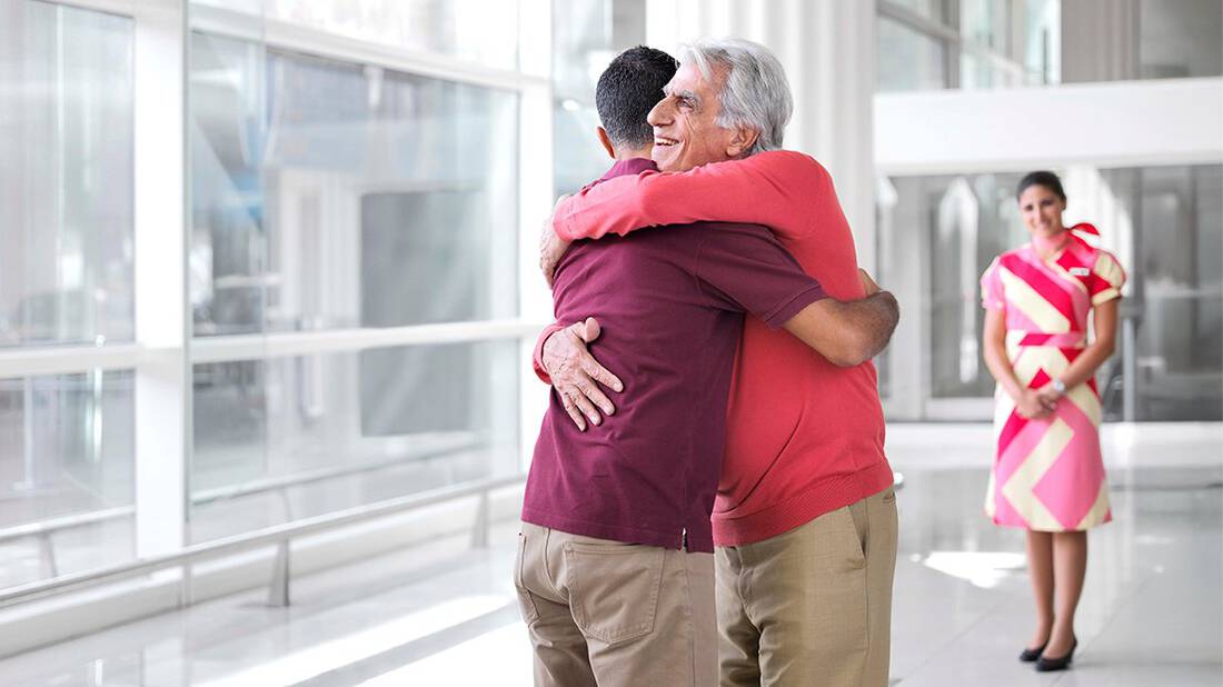 a son hugging his elderly dad with a marhaba representative standing in the background