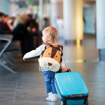 toddler dragging his luggage through the airport while carrying a lion backpack